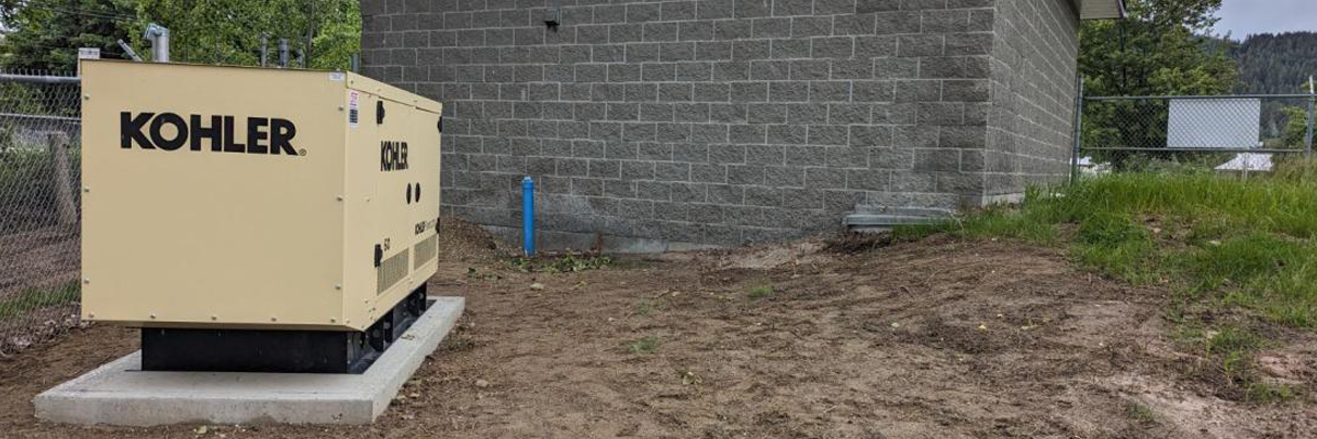 Un grand générateur fixe de secours Kohler de couleur beige est installé sur une dalle de béton à l'extérieur du bâtiment de la station de traitement de l'eau de Grindrod, qui est constituée de briques grises.
