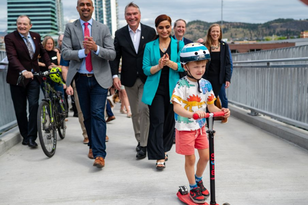 Les membres de la collectivité traversent une passerelle pour piétons au-dessus d’une autoroute, dont une personne avec un vélo et un enfant en trottinette.