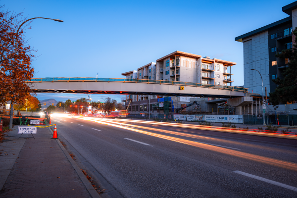 Une passerelle pour piétons au-dessus d’une autoroute, avec des bâtiments à proximité.