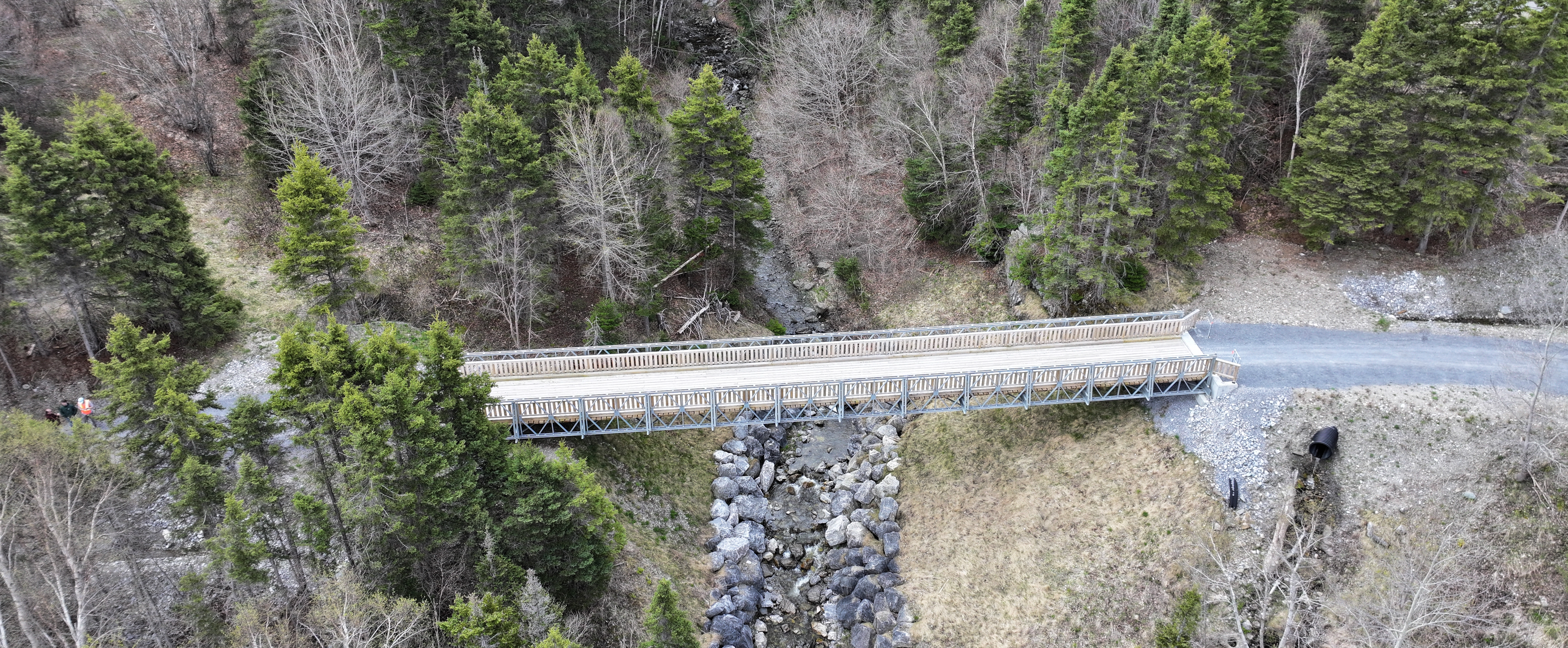 Vue aérienne d’un pont piétonnier en bois et en métal qui enjambe un ponceau large mais peu profond
