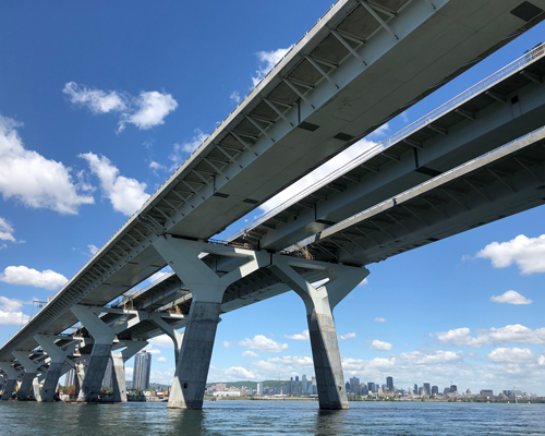 Vue aérienne d’un pont à haubans moderne à côté d’un pont à poutres triangulées plus ancien, enjambant une large rivière.