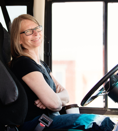 Une conductrice d’autobus assise dans un autobus et souriante.