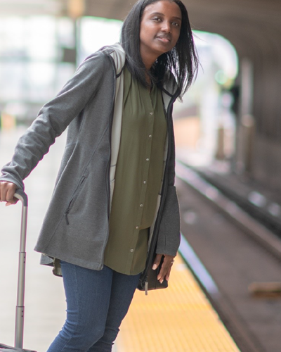 Une femme debout sur un quai de métro se penche vers l’avant pour chercher le train. Elle tient une valise.