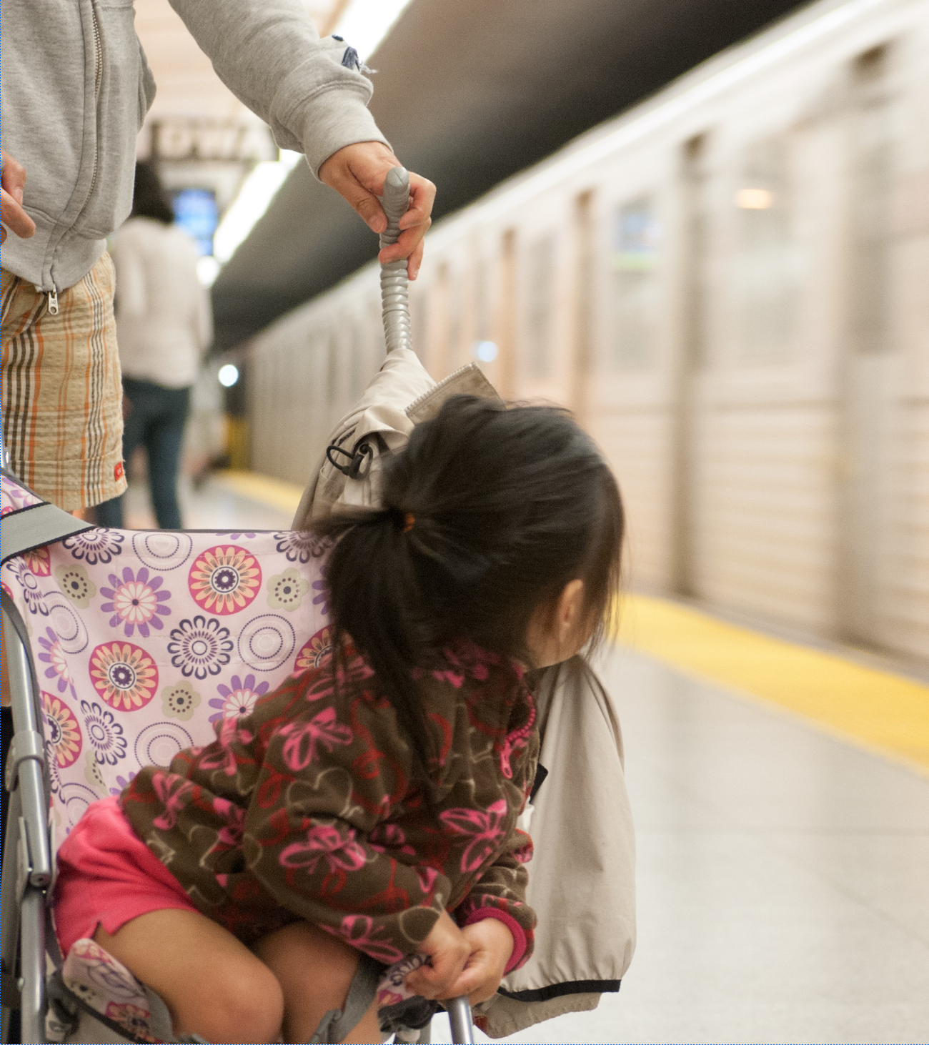 Une jeune fille est poussée dans une poussette sur un quai de métro alors qu'un train passe.