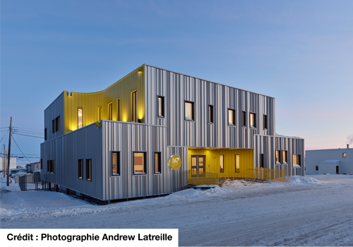 1.	Un bâtiment moderne illuminé sous un ciel clair au crépuscule, avec de la neige recouvrant le sol.