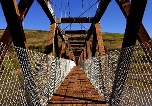 Pont pour piéton en métal, vu d’une extrémité du pont. Clôture en métal des deux côtés du pont