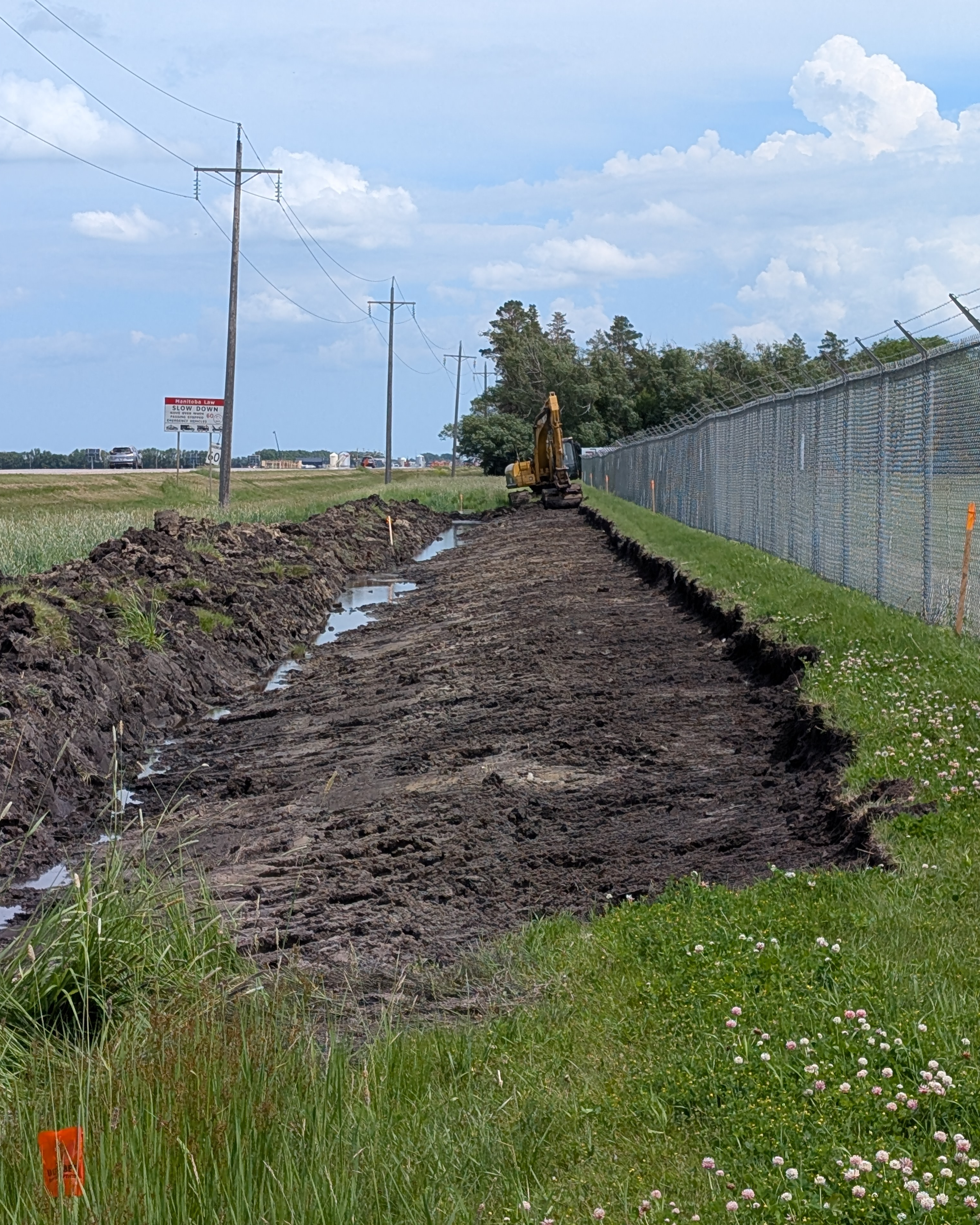 Gazon déterré, avec une excavatrice au loin et une clôture grillagée à droite.